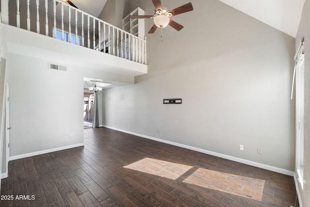 unfurnished living room featuring ceiling fan with notable chandelier, dark wood-type flooring, and a high ceiling