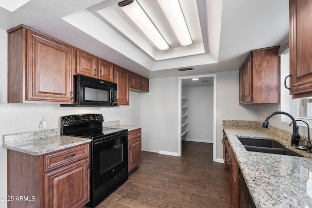 kitchen featuring a tray ceiling, sink, light stone counters, and black appliances