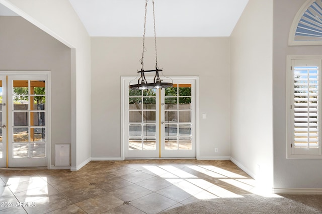 unfurnished dining area featuring high vaulted ceiling, a notable chandelier, and a wealth of natural light