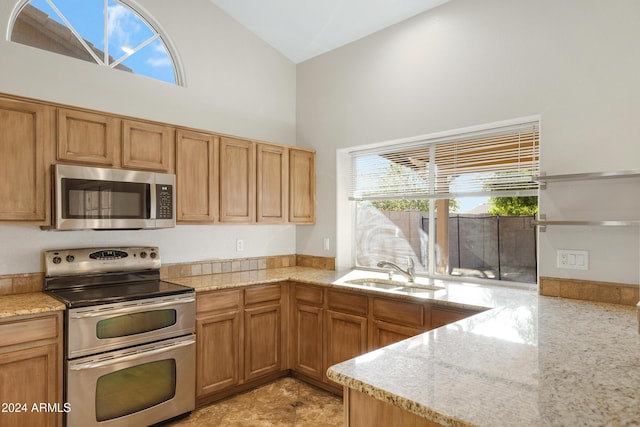 kitchen with light stone countertops, sink, high vaulted ceiling, and stainless steel appliances