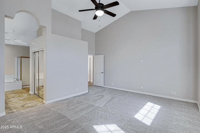 carpeted empty room featuring ceiling fan, high vaulted ceiling, arched walkways, and baseboards