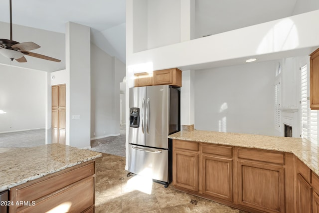 kitchen with high vaulted ceiling, brown cabinets, stainless steel fridge, and light stone counters