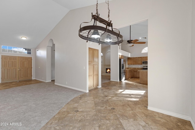 unfurnished dining area with arched walkways, light carpet, ceiling fan, high vaulted ceiling, and baseboards