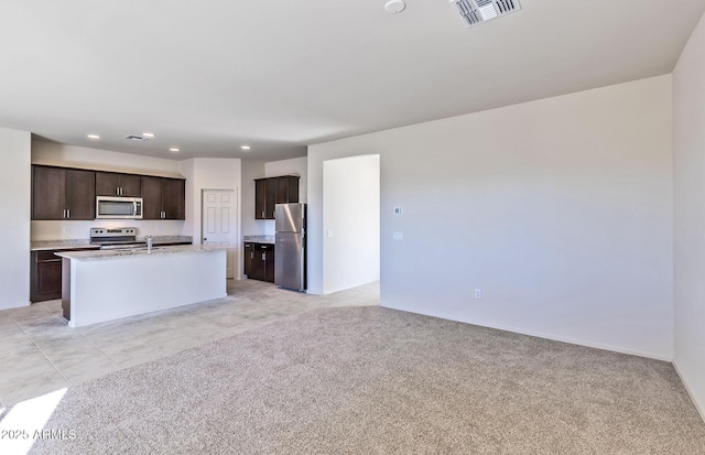 kitchen featuring sink, light colored carpet, an island with sink, and appliances with stainless steel finishes