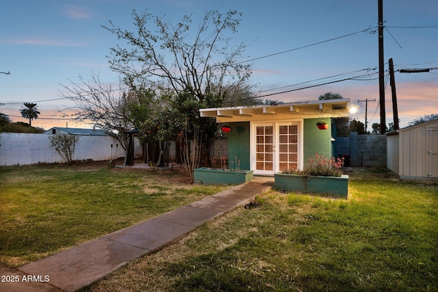 view of front of property with a front lawn, a storage unit, french doors, and fence