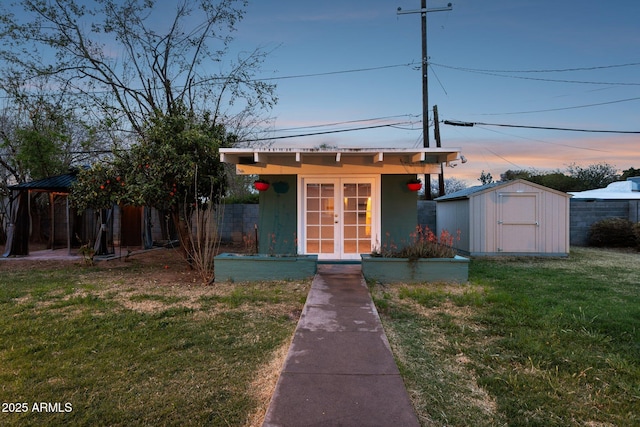 view of front facade featuring french doors, a front lawn, an outdoor structure, and fence