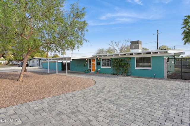 view of front of home with an attached carport, fence, cooling unit, a chimney, and decorative driveway