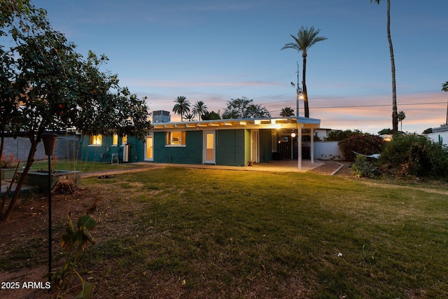 back of property at dusk with a lawn, a patio, and an attached carport