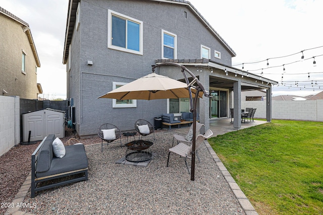 back of house featuring an outdoor living space with a fire pit, a patio, a fenced backyard, a storage unit, and a lawn