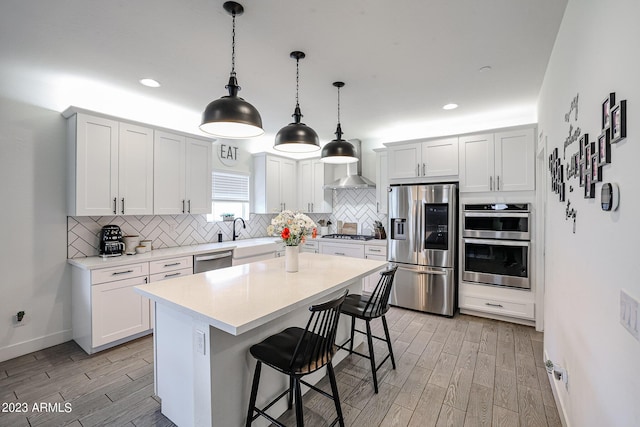 kitchen featuring a kitchen bar, tasteful backsplash, light wood-style floors, stainless steel appliances, and wall chimney exhaust hood