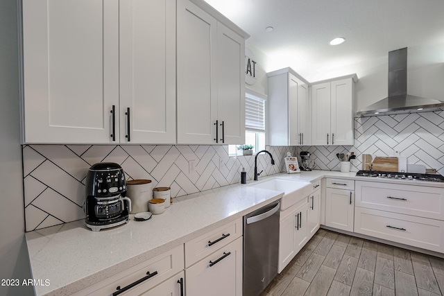 kitchen featuring a sink, wall chimney exhaust hood, appliances with stainless steel finishes, and white cabinetry