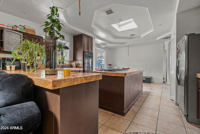 kitchen featuring a center island, a tray ceiling, stainless steel appliances, and dark brown cabinetry