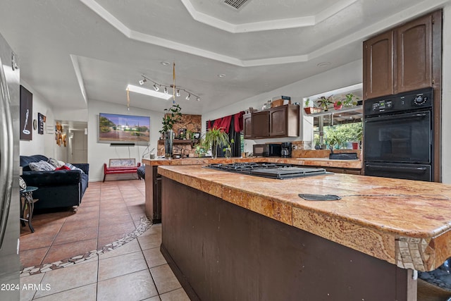 kitchen with dark brown cabinets, black appliances, a kitchen island, a tray ceiling, and light tile patterned flooring