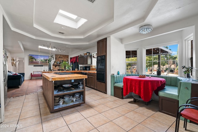 kitchen featuring dark brown cabinets, light tile patterned floors, wood counters, a tray ceiling, and a skylight