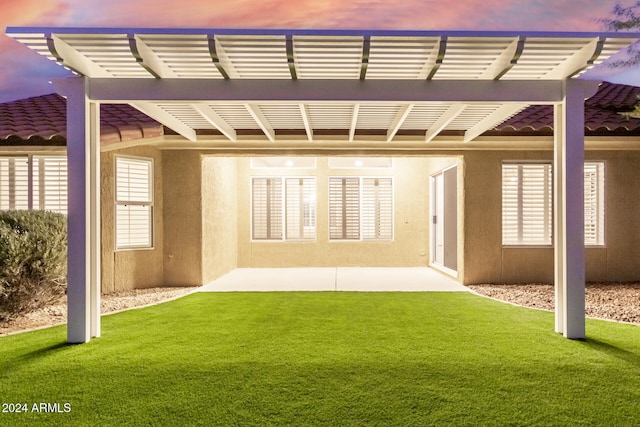 back house at dusk featuring a patio area, a lawn, and a pergola