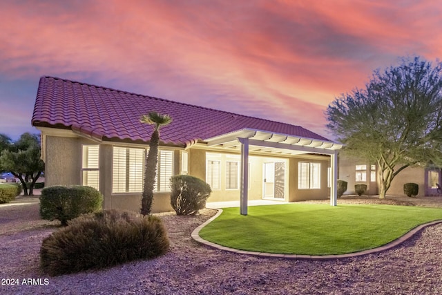 back house at dusk with a patio area, a yard, and a pergola