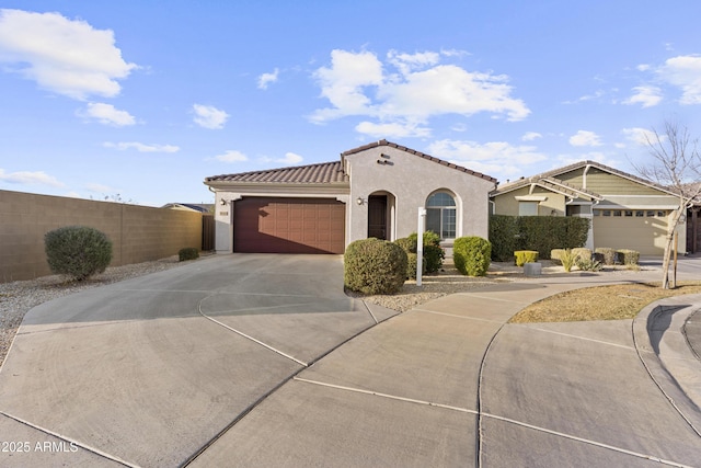 mediterranean / spanish home with a garage, concrete driveway, a tile roof, fence, and stucco siding