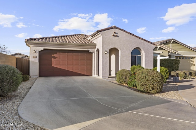 mediterranean / spanish-style house with a garage, fence, driveway, a tiled roof, and stucco siding