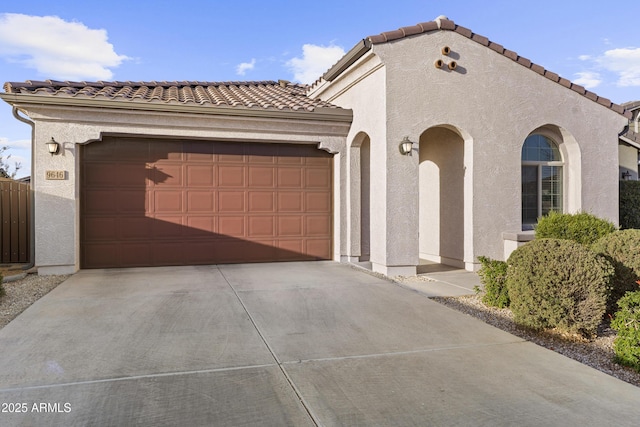 mediterranean / spanish house with a garage, concrete driveway, a tiled roof, and stucco siding