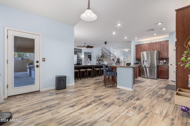 kitchen featuring stainless steel refrigerator with ice dispenser, light stone counters, a breakfast bar, decorative light fixtures, and light hardwood / wood-style floors