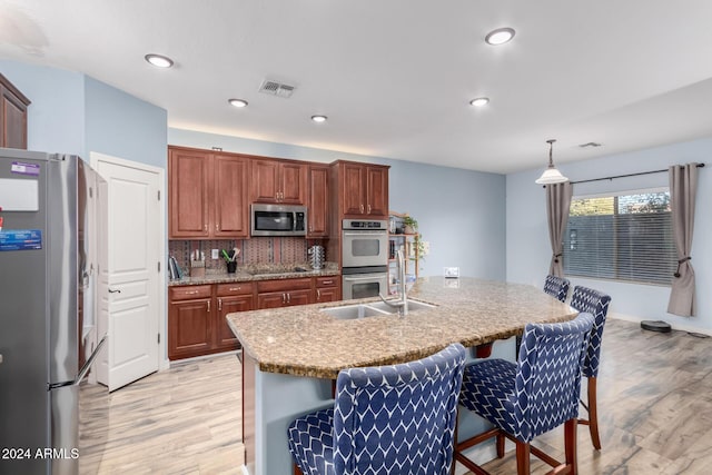 kitchen with decorative backsplash, appliances with stainless steel finishes, light wood-type flooring, decorative light fixtures, and a center island with sink