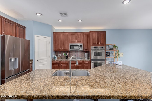 kitchen featuring a large island with sink, backsplash, appliances with stainless steel finishes, and sink