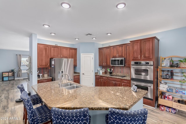 kitchen featuring sink, an island with sink, stainless steel appliances, and light wood-type flooring