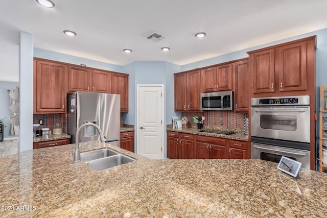 kitchen with light stone countertops, appliances with stainless steel finishes, tasteful backsplash, and sink