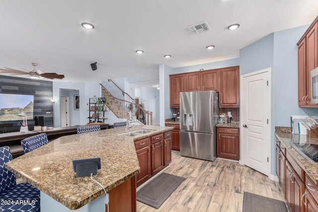 kitchen featuring light stone counters, a center island with sink, light hardwood / wood-style floors, and appliances with stainless steel finishes