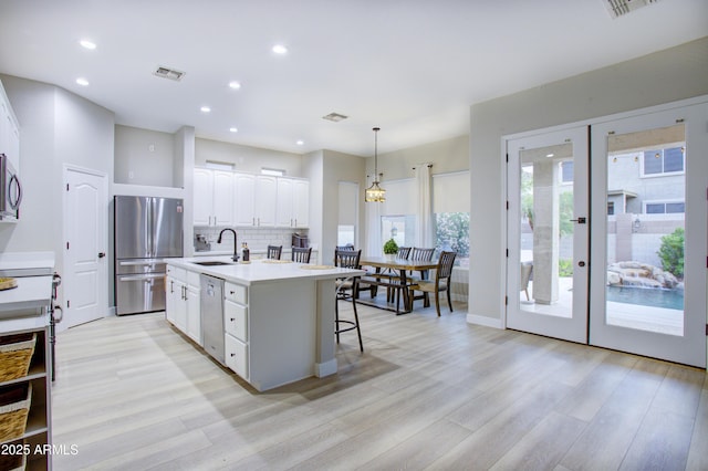 kitchen featuring stainless steel appliances, french doors, a sink, a center island with sink, and white cabinetry