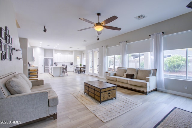 living room featuring baseboards, visible vents, a ceiling fan, and a wealth of natural light