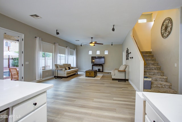 living area with light wood finished floors, baseboards, visible vents, a ceiling fan, and stairway