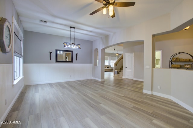 interior space featuring stairway, ceiling fan with notable chandelier, wainscoting, arched walkways, and visible vents