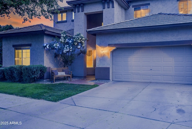view of front facade with stucco siding, driveway, a tiled roof, and a garage
