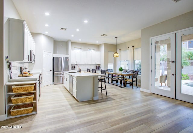 kitchen featuring light wood finished floors, stainless steel appliances, backsplash, visible vents, and a sink