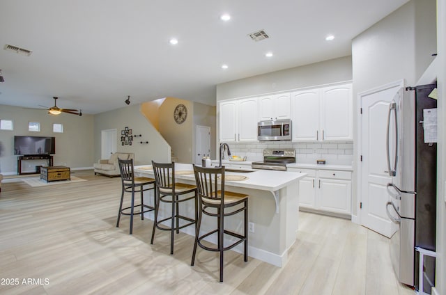 kitchen featuring white cabinets, a kitchen breakfast bar, visible vents, light wood-style floors, and appliances with stainless steel finishes