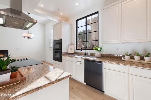 kitchen featuring sink, white cabinets, light stone countertops, island range hood, and black appliances