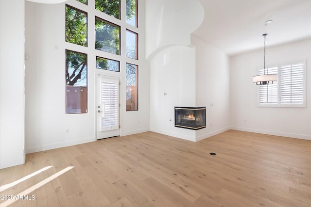 unfurnished living room with a multi sided fireplace, a high ceiling, a healthy amount of sunlight, and light hardwood / wood-style flooring