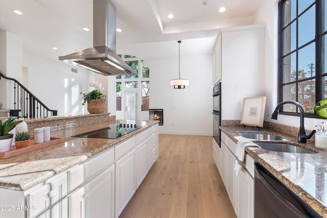 kitchen with light stone counters, island range hood, black appliances, light wood-type flooring, and white cabinetry