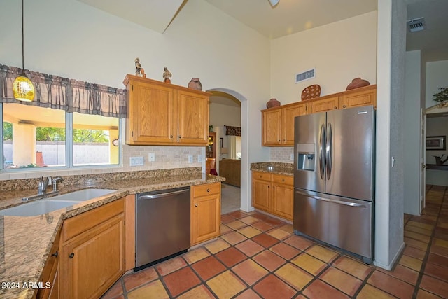 kitchen with appliances with stainless steel finishes, tasteful backsplash, sink, decorative light fixtures, and a high ceiling