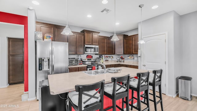11742 W Chase Ln, Avondale, AZ 85323 - kitchen with appliances with stainless steel finishes, dark brown cabinets, a sink, light countertops, and a kitchen island with sink