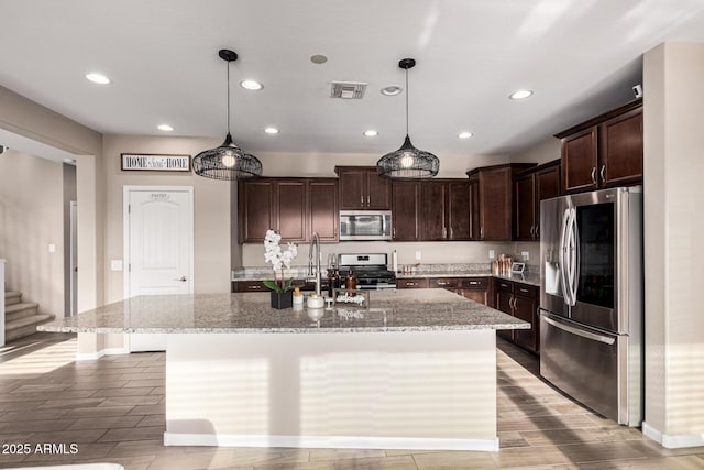 kitchen with light stone countertops, appliances with stainless steel finishes, decorative light fixtures, a kitchen island with sink, and dark brown cabinets