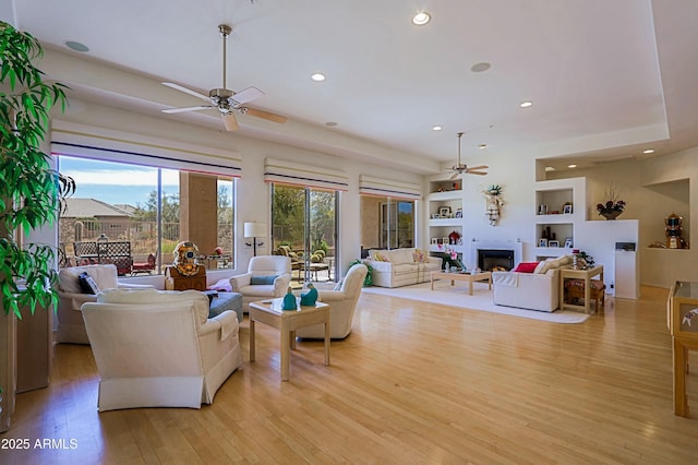 living area with ceiling fan, recessed lighting, built in features, light wood-style floors, and a lit fireplace