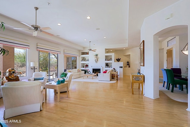 living area with light wood finished floors, built in features, ceiling fan, a fireplace, and recessed lighting