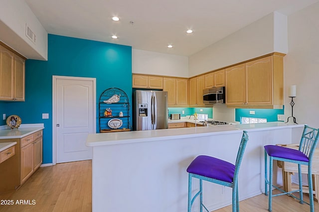 kitchen featuring a peninsula, a breakfast bar, appliances with stainless steel finishes, light brown cabinetry, and light wood finished floors