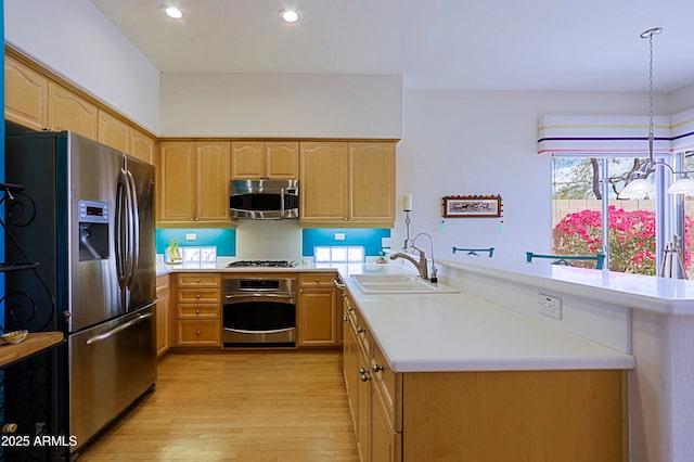 kitchen with light brown cabinets, stainless steel appliances, a peninsula, a sink, and light countertops