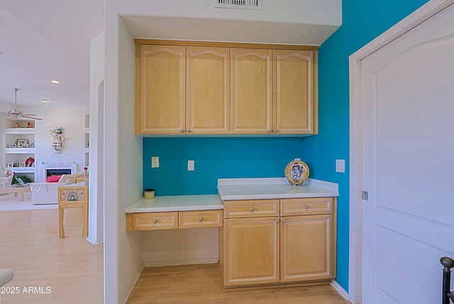 kitchen with built in desk, a fireplace, light wood-style flooring, and light brown cabinetry