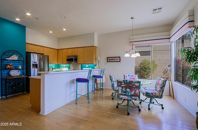 kitchen with stainless steel appliances, light countertops, visible vents, light wood-style floors, and a peninsula