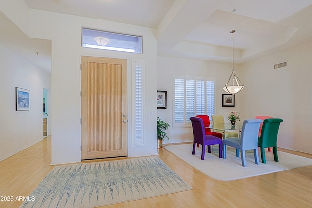 foyer entrance with a raised ceiling, wood finished floors, visible vents, and baseboards