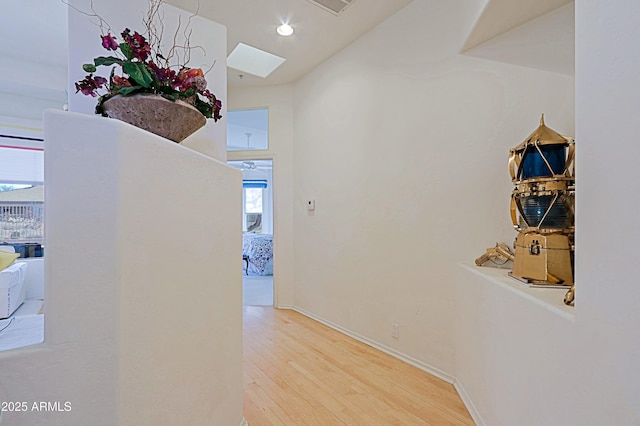 hallway with a skylight, recessed lighting, wood finished floors, and baseboards